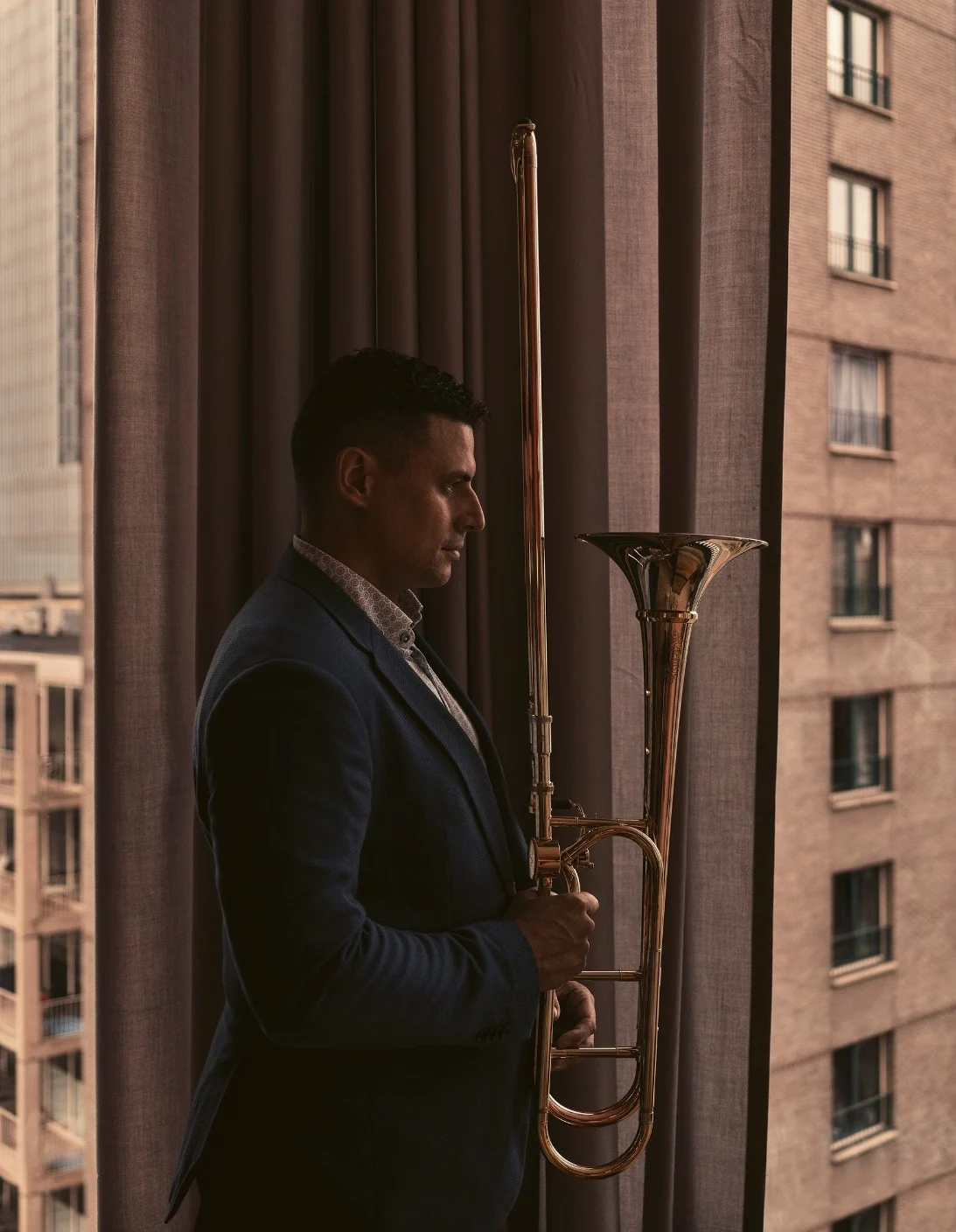 Alejandro holding his trombone beside a window in Rotterdam