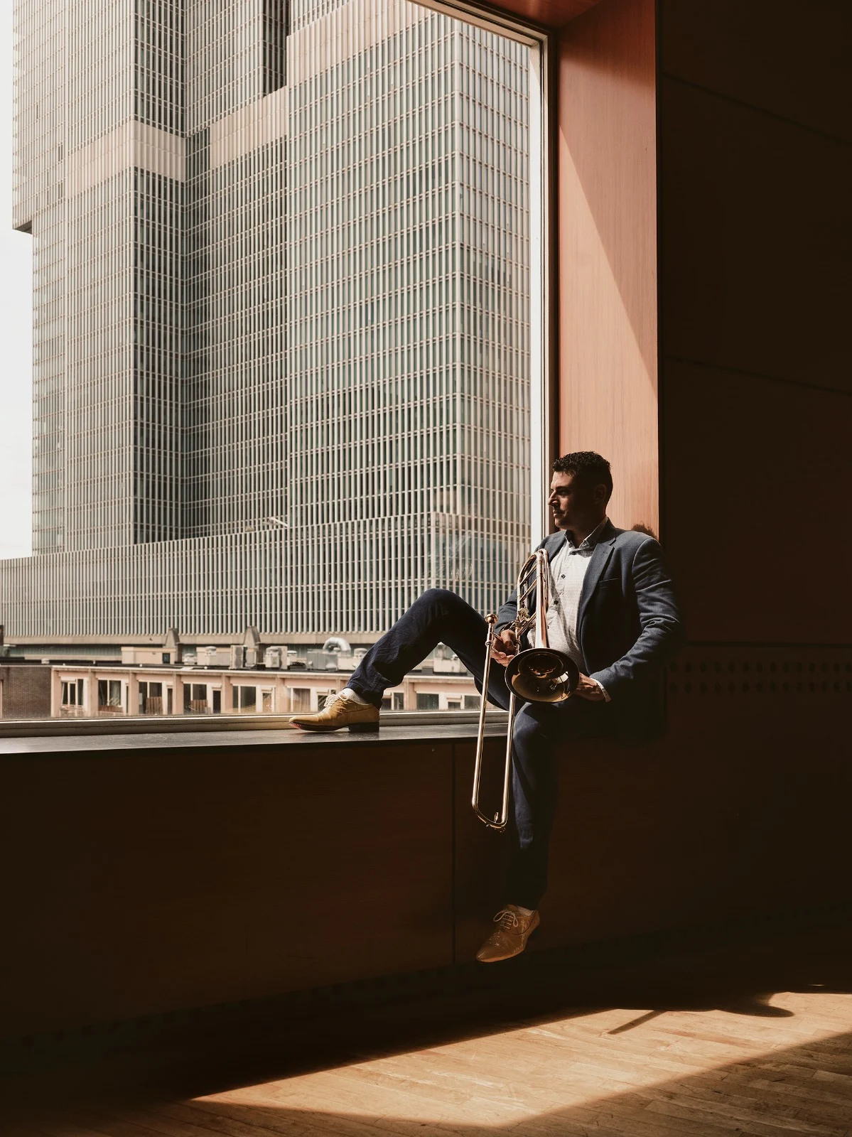 Alejandro seated beside a window with his trombone
